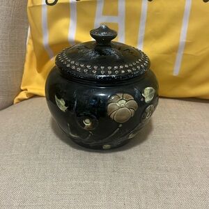 Black jar with lid and flowers painted on it.